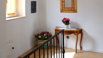 Una escalera con techo de vigas de madera, un espejo en la pared, una pequeña mesa con un florero y una ventana con cortinas.