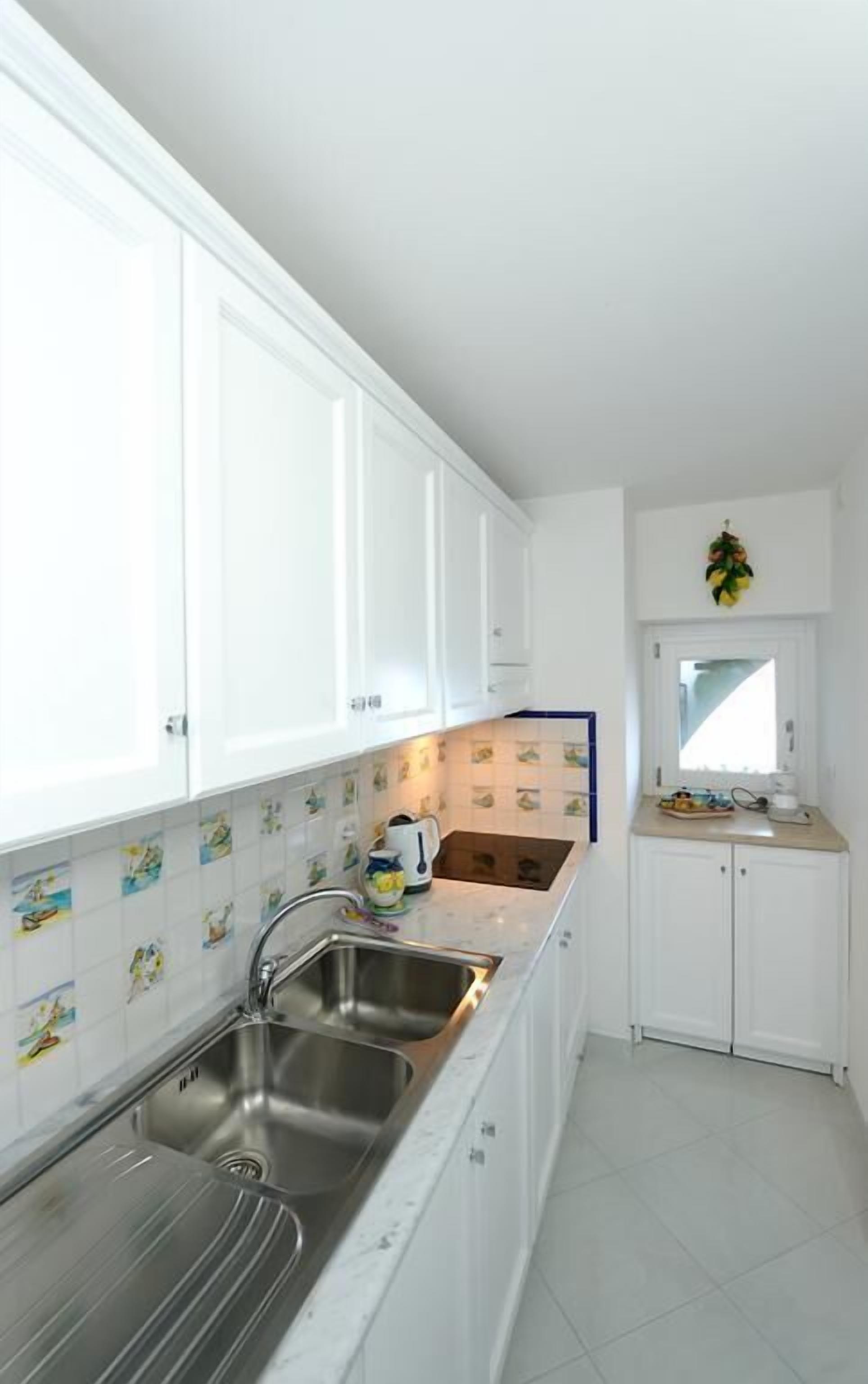 A modern kitchen with white cabinets, a stainless steel sink, and a window above the sink.