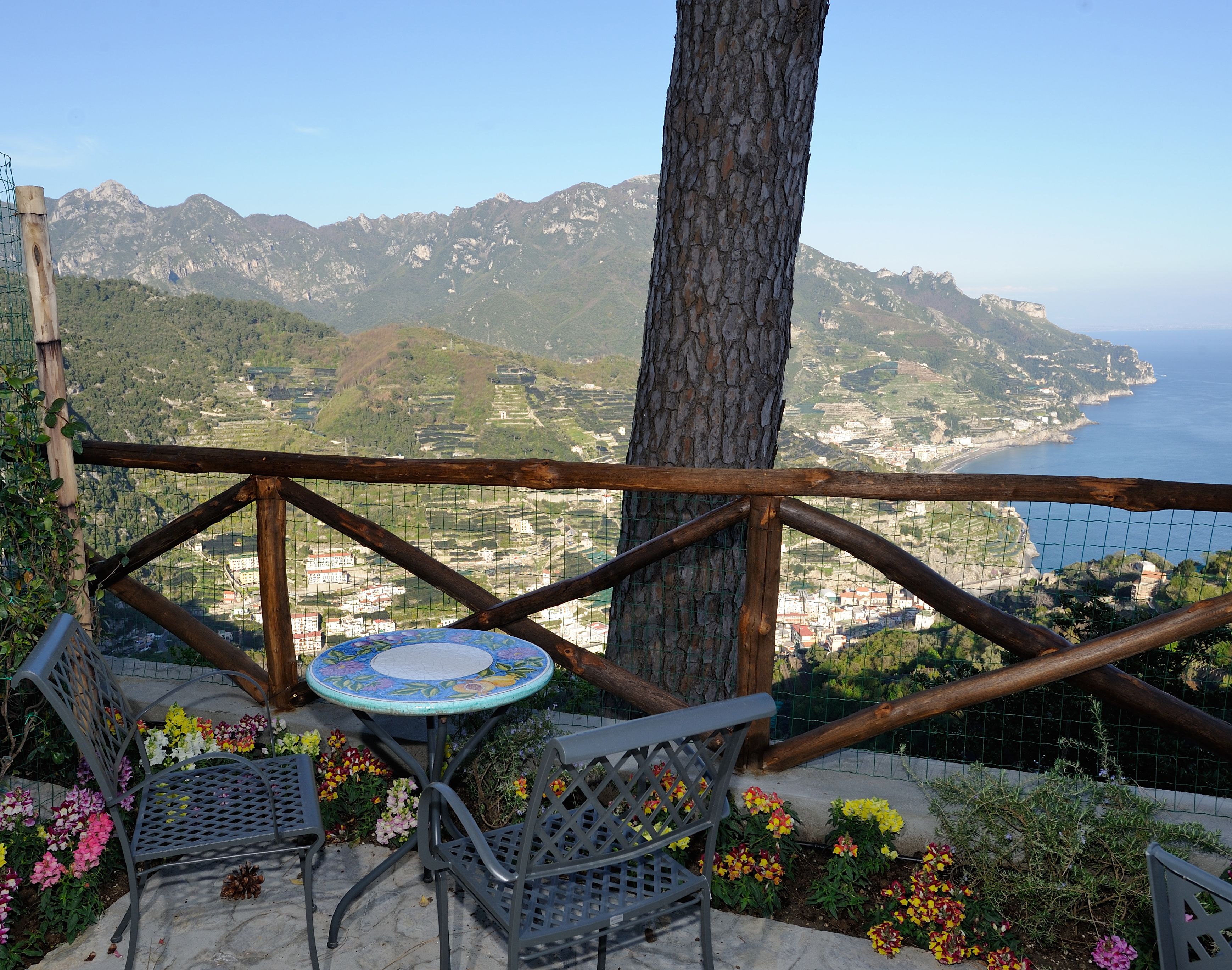 Una terraza con mesa y sillas, con vista a un paisaje costero con montañas y el mar.