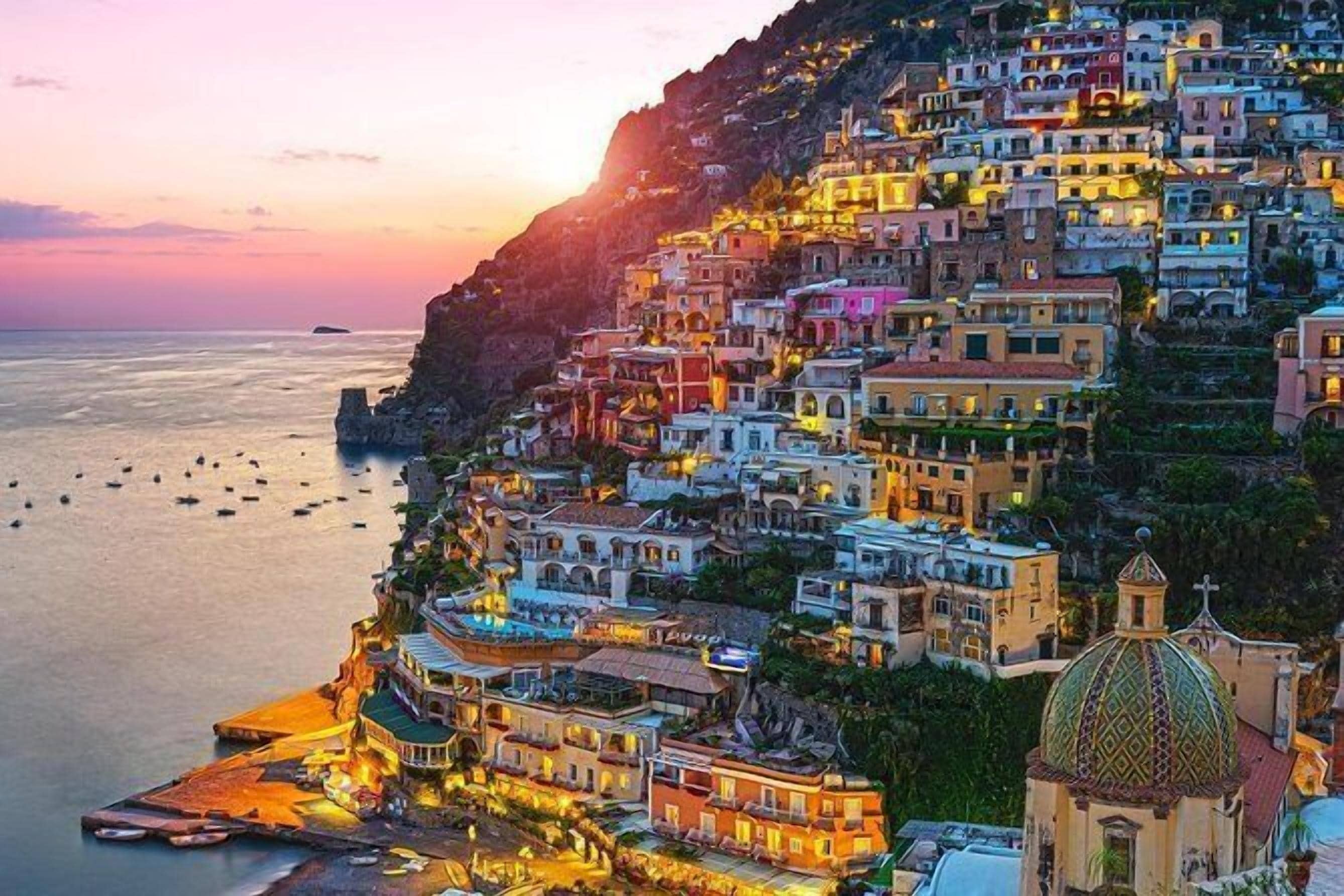 A coastal town with colorful buildings, a prominent church with a green dome, and boats on the water.