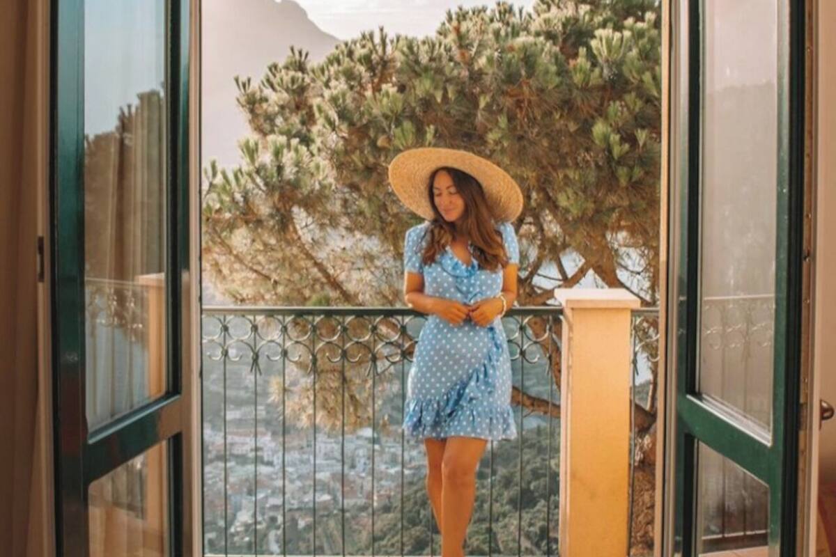 A woman standing in a doorway with a view of a mountainous landscape and a tree.