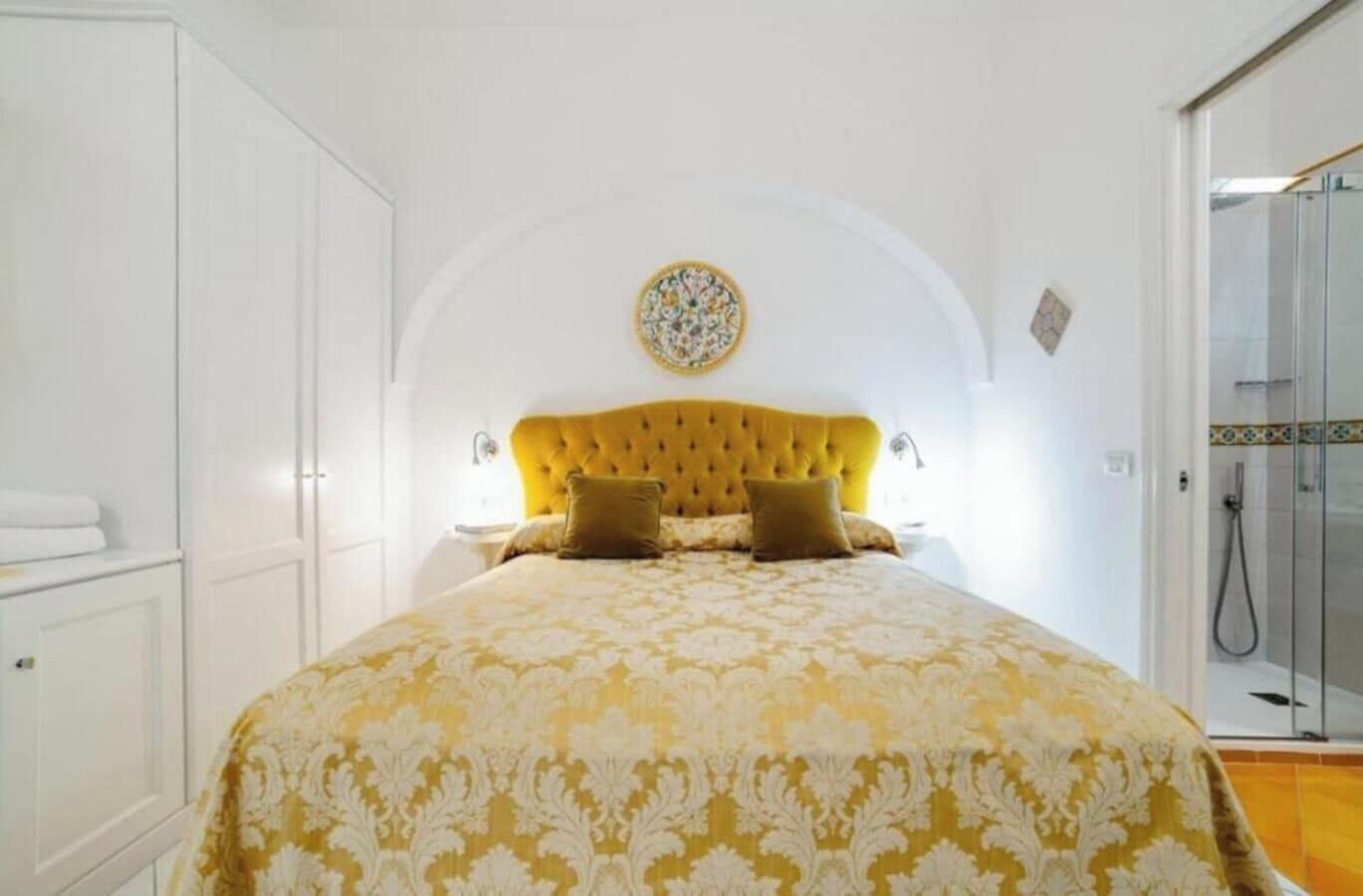 A bedroom with a tufted headboard, a patterned bedspread, and a decorative wall piece.