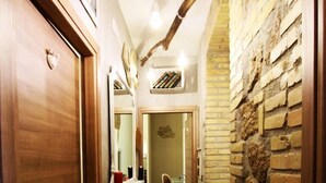 Un pasillo estrecho con una puerta de madera a la izquierda, una pared de piedra a la derecha y un espejo sobre la puerta.