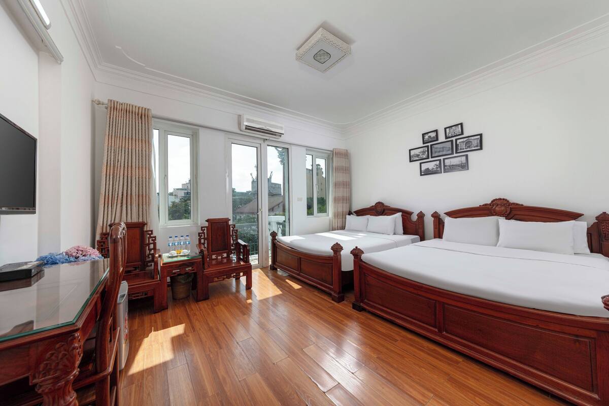 A hotel room with two wooden beds, a desk with a chair, a television, and a window with curtains.