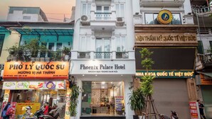 A hotel with a sign reading "Phoenix Palace Hotel" and another sign for "PHO LY QUOC SU" with a menu.