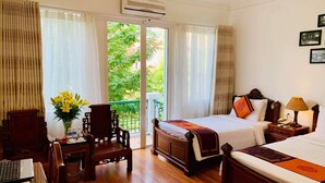 A hotel room with a bed, a desk with a laptop, a chair, and a view of greenery through the window.
