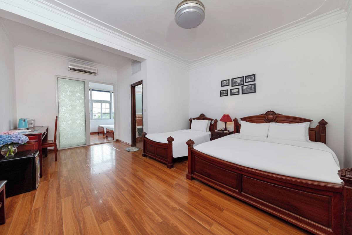 A hotel room with two wooden beds, a desk with a lamp, a chair, and a small table with a vase.
