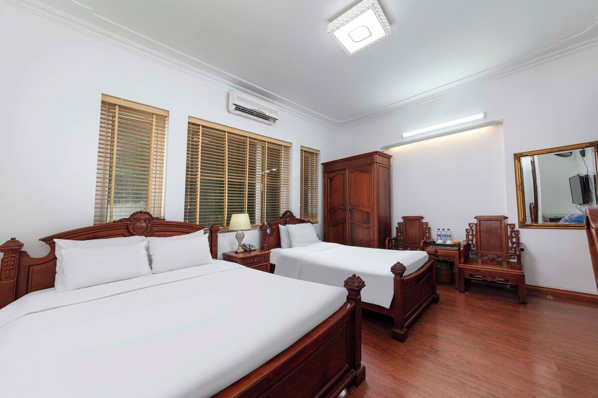 A hotel room with two wooden beds, a wardrobe, a mirror, and a nightstand.