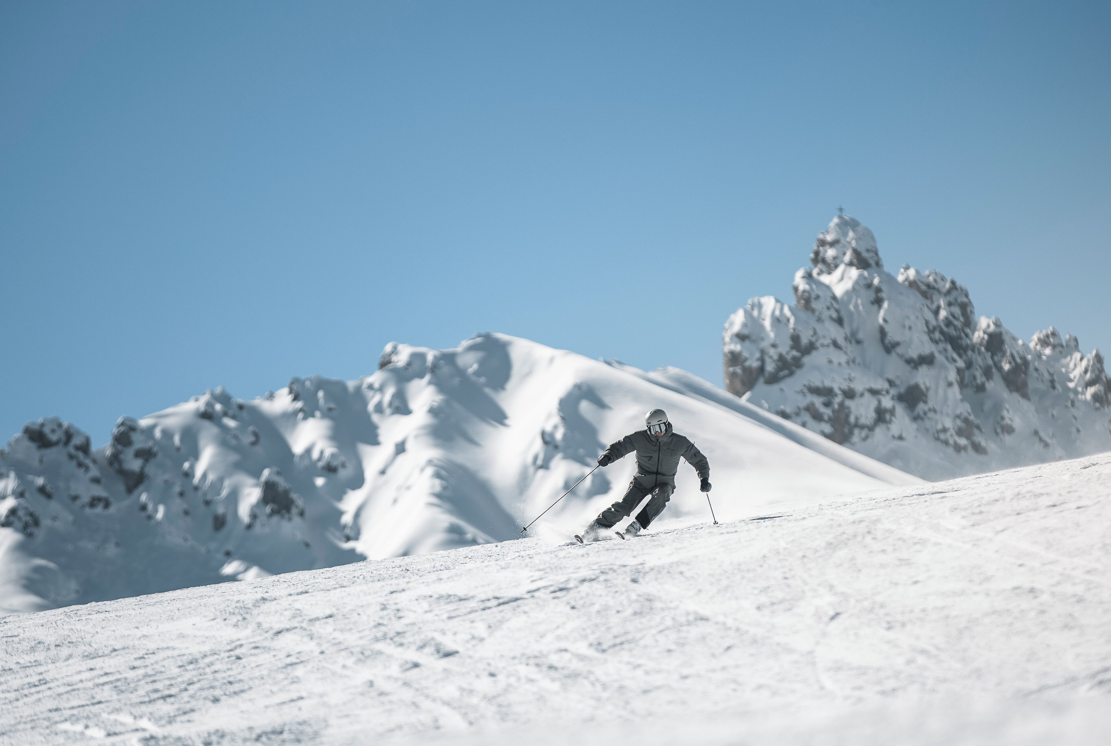 A person skiing down a snowy slope with mountains in the background.