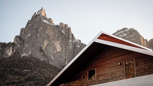 A wooden cabin with a sloped roof, set against a mountainous backdrop. - La Paula Apartments & Suites (Castelrotto)