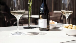 A table with a bottle of wine, two wine glasses, a vase with yellow flowers, and a bowl of olives. - La Paula Apartments & Suites (Castelrotto)