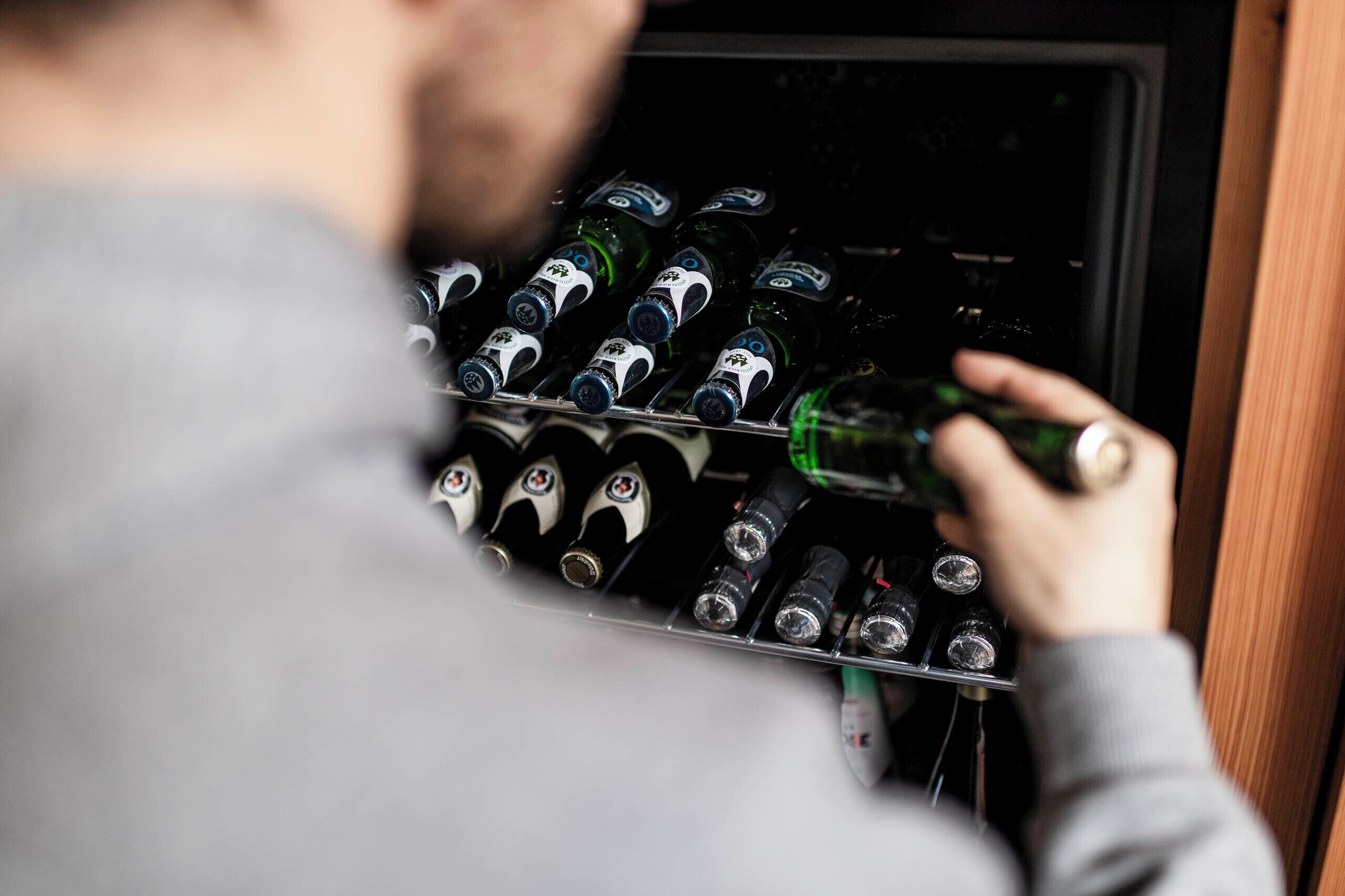 A person selecting a bottle from a refrigerator stocked with various bottles.