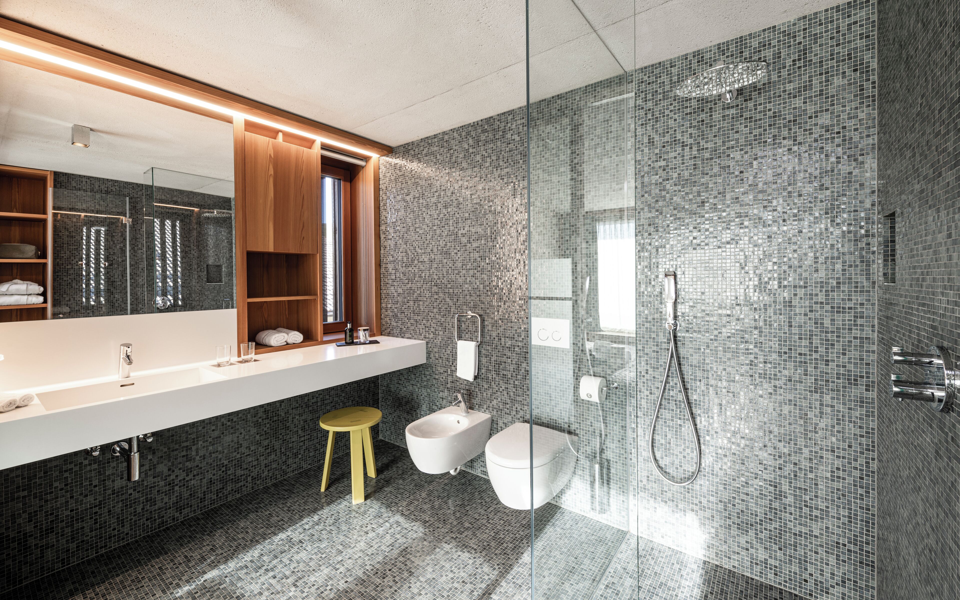 Ein modernes Badezimmer mit einem großen Spiegel, einem Holzkosmetikschrank und einem Duschbereich mit Mosaikfliesen.
