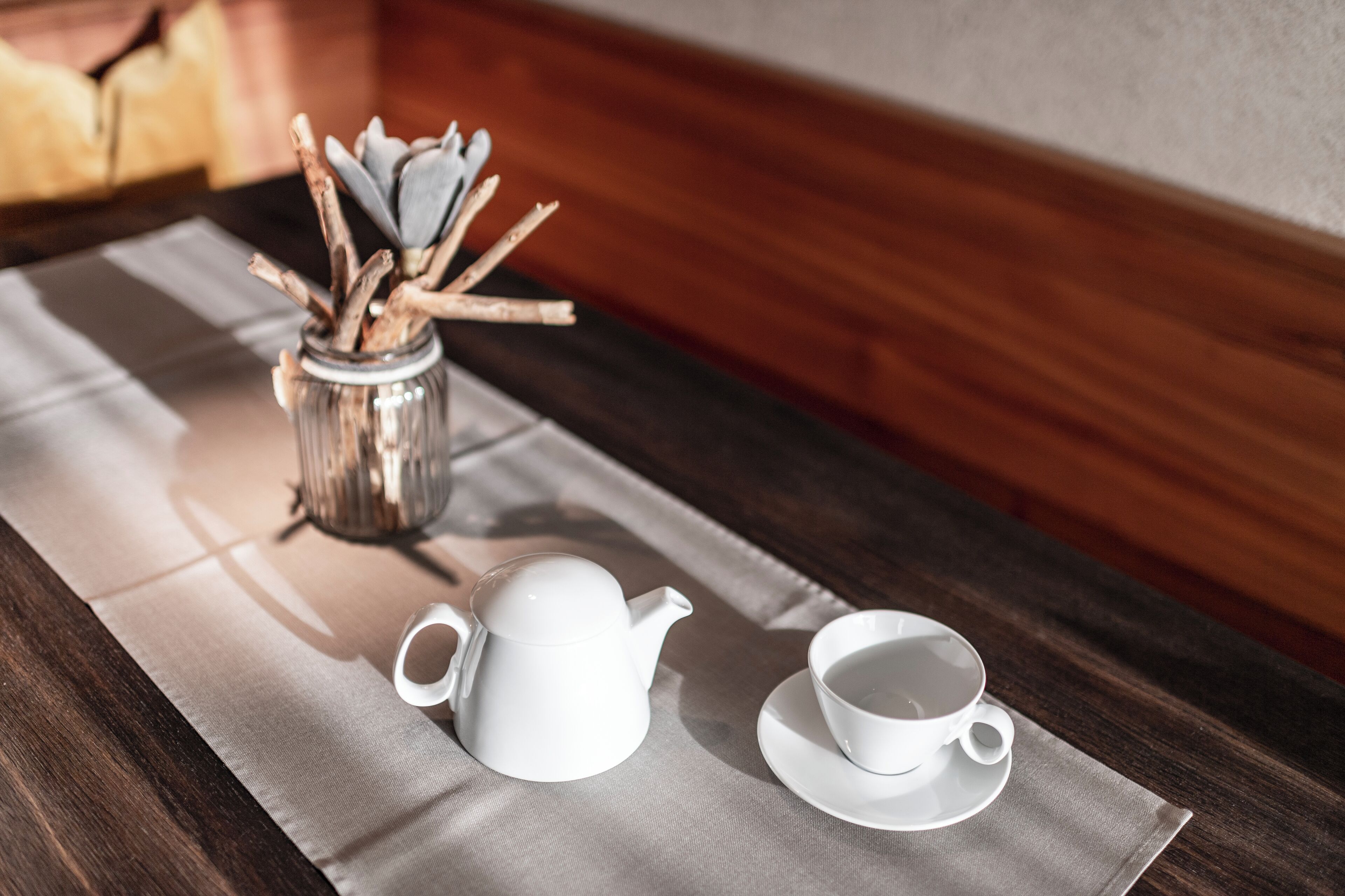 Ein Holztisch mit einem weißen Teekessel und einer Tasse auf einer grauen Tischmatte.