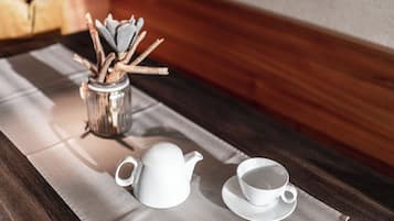Ein Holztisch mit einem weißen Teekessel und einer Tasse auf einer grauen Tischmatte.