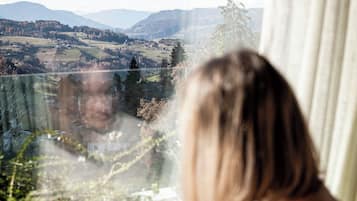 Una persona sentada junto a una ventana con vistas a un valle y montañas a lo lejos.