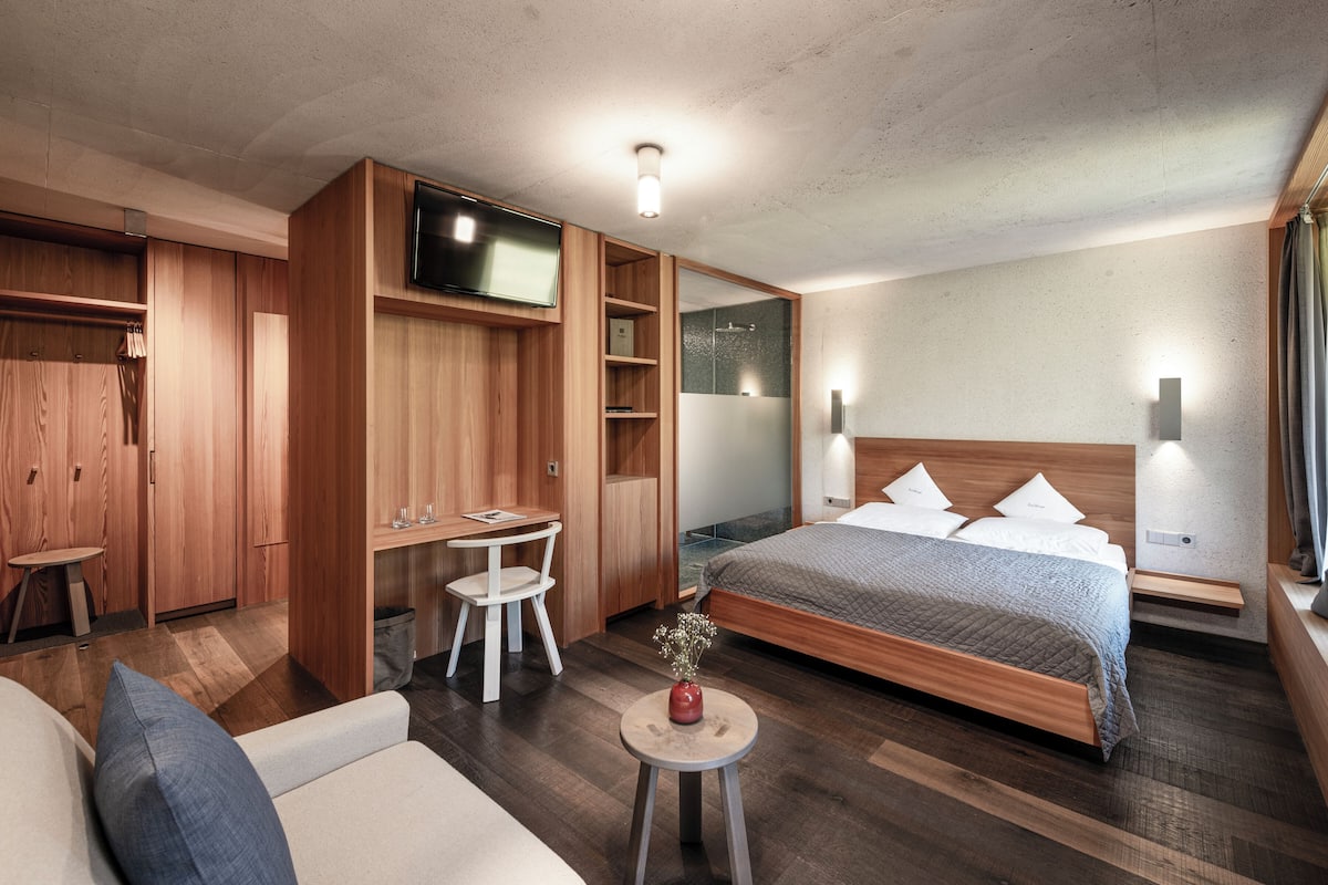 A modern hotel room with a bed, a TV, a desk, and a seating area.