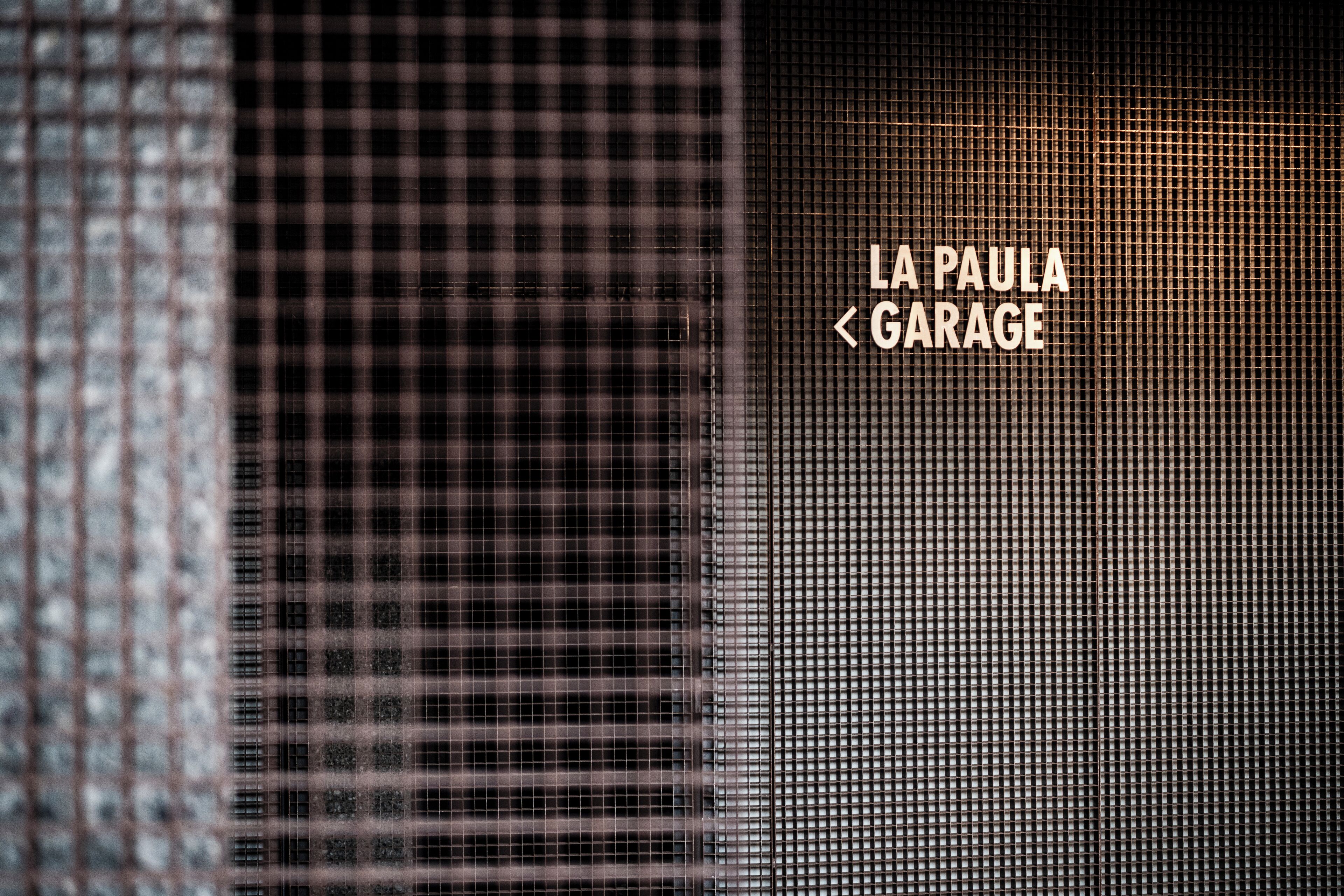 Ein Detailfoto einer Gebäudefassade mit einem gitterartigen Muster und dem Schriftzug "LA PAULA < GARAGE".