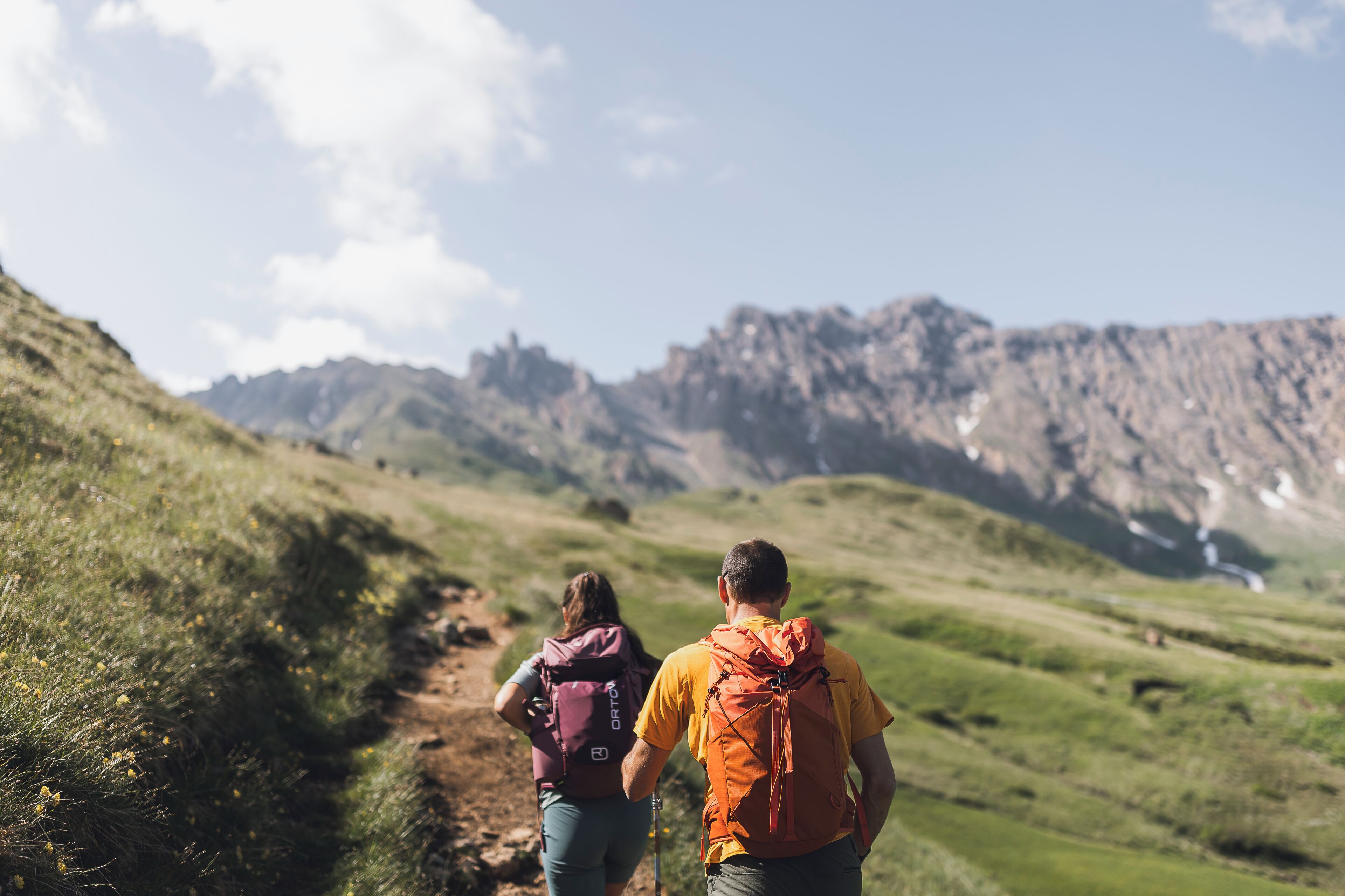 Deux randonneurs sur un sentier, avec des montagnes en arrière-plan.
