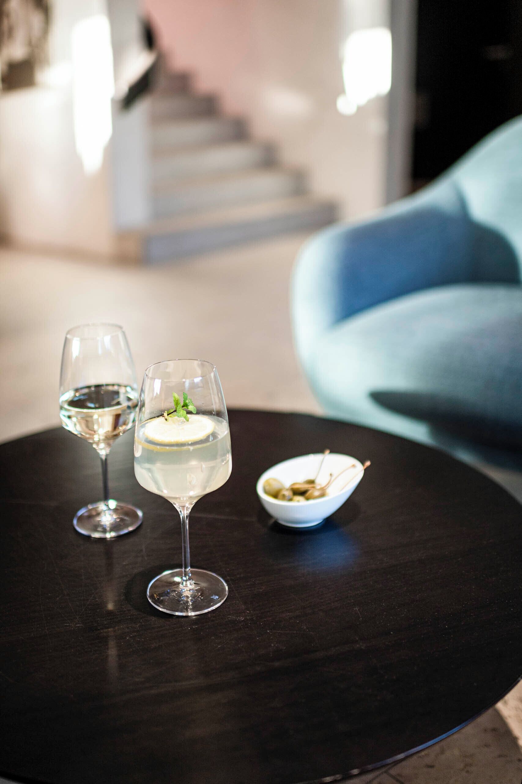Two glasses of white wine on a round table with a bowl of olives.