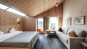 A room with a wooden ceiling, a bed, a sofa, a small table, and a window with curtains. - La Paula Apartments & Suites (Castelrotto)