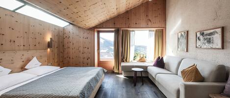 A room with a wooden ceiling, a bed, a sofa, a small table, and a window with curtains.