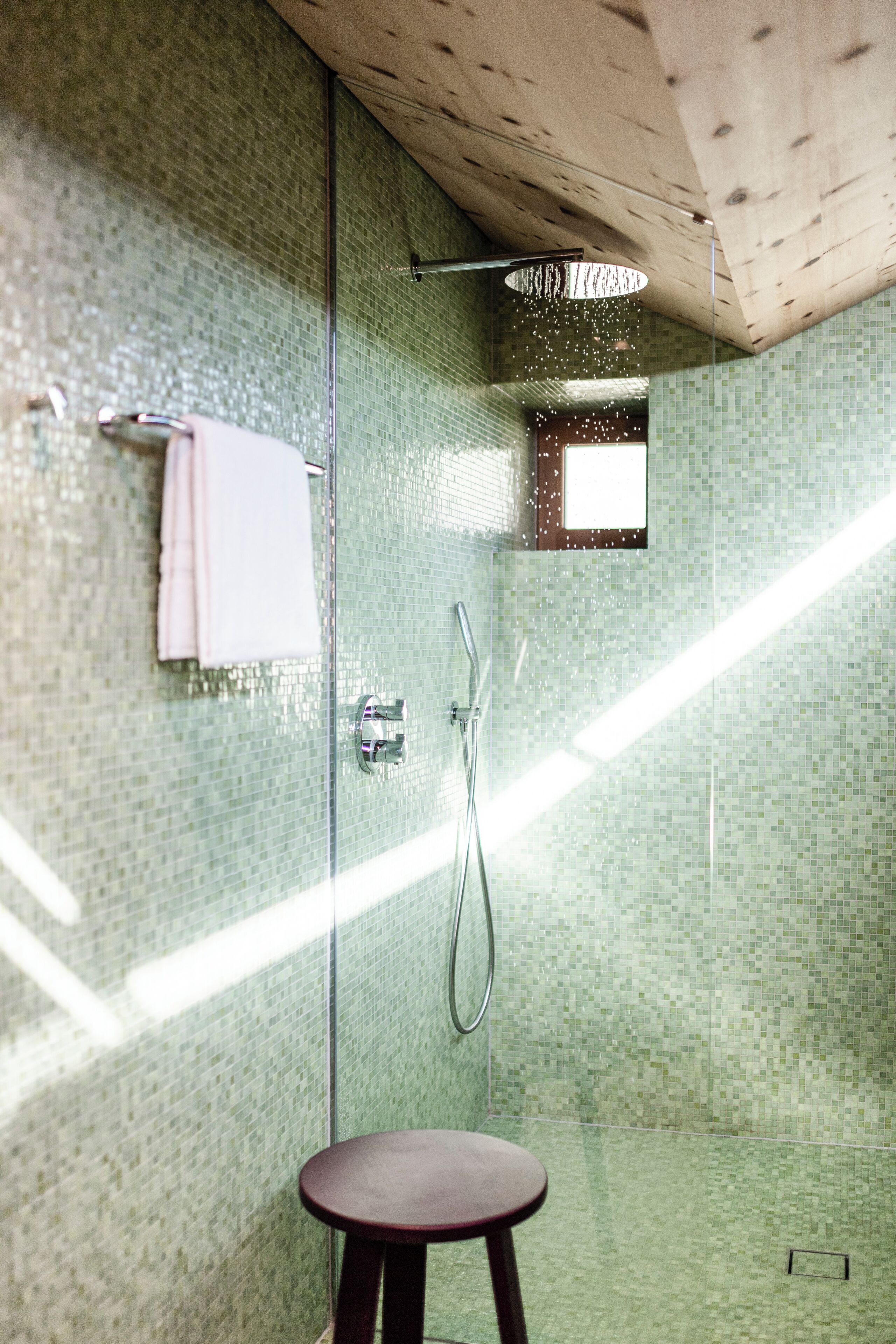 Un baño moderno con cabina de ducha de vidrio, techo de madera y un pequeño taburete.