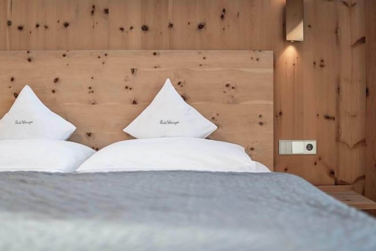 A bed with white bedding and two pillows, a wooden headboard, and a wall-mounted light fixture.