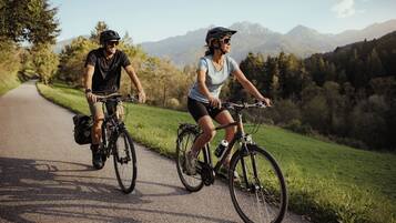 Dos personas andando en bicicleta por un camino pavimentado, rodeado de vegetación y montañas.