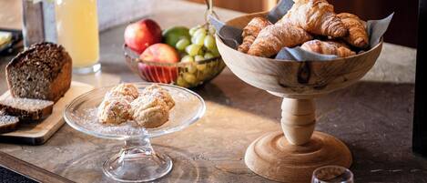A breakfast setting with croissants, muffins, and a bowl of fruit on a marble countertop.