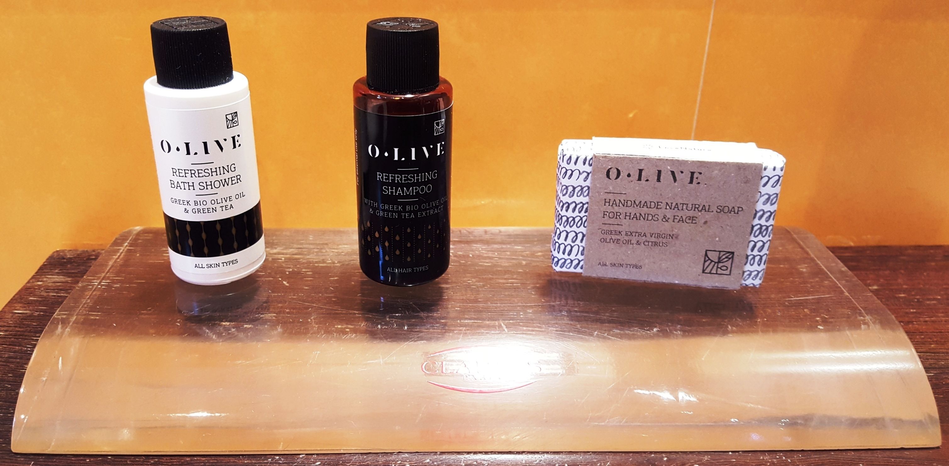 Three O.LIVE products: a refreshing bath shower, a refreshing shampoo, and handmade natural soap for hands and face.
