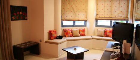 A living room with a sofa, a coffee table, a TV, and a window with a curtain.