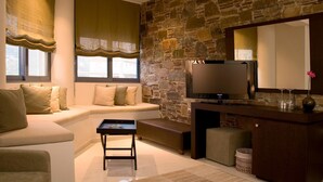A modern living room with a stone wall, a large flat-screen TV, a sofa, a coffee table, and a bench. - Sea Sight Hotel (Markopoulo Mesogaias)
