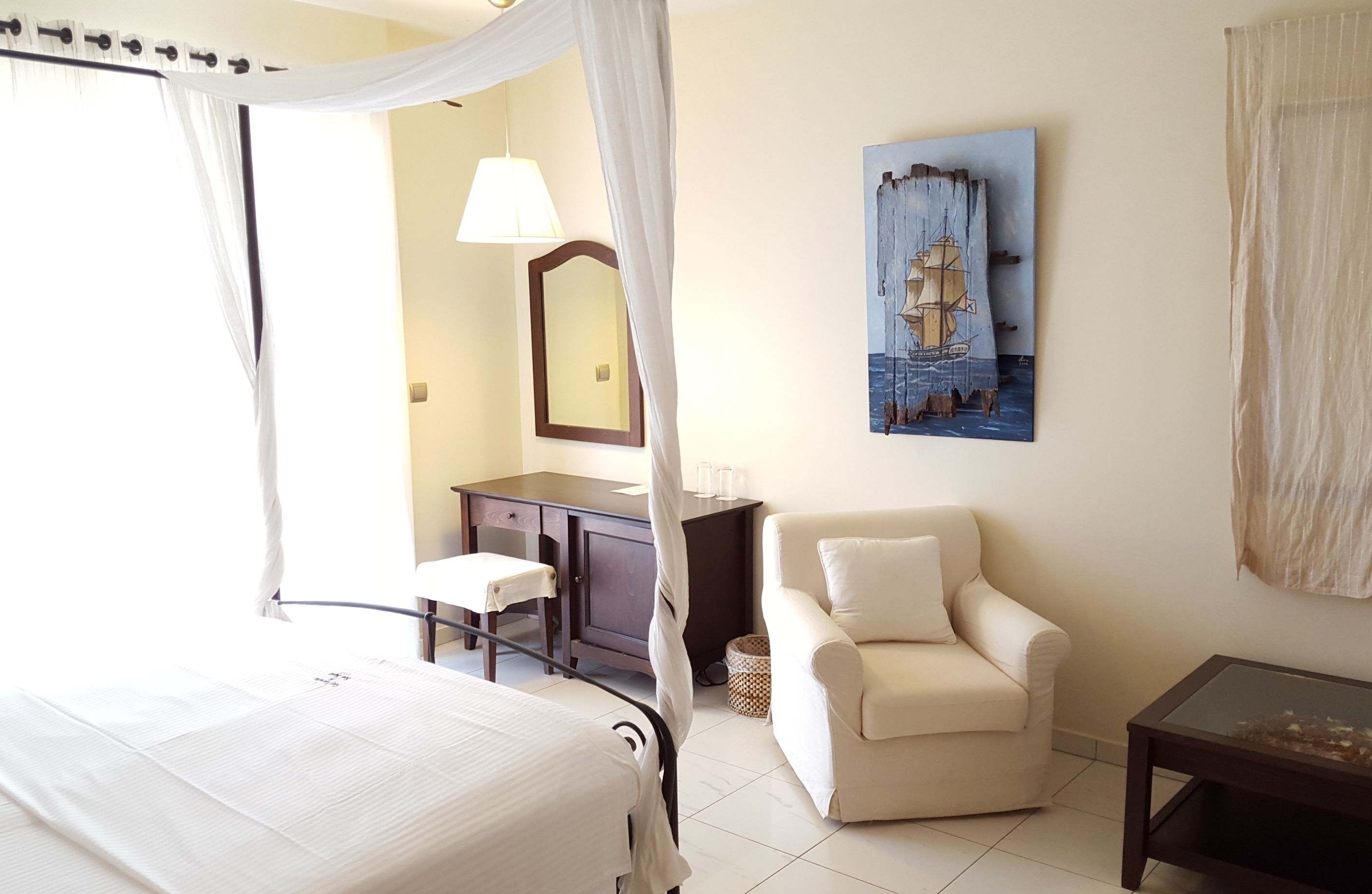 A bedroom with a bed, a desk, a chair, a bedside table, a lamp, and a painting on the wall.