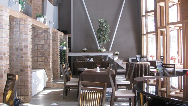 A restaurant with brick walls, wooden beams, and large windows. Tables and chairs are arranged for dining.