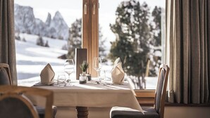 Mesa de comedor dispuesta con vistas a montañas nevadas y árboles a través de amplios ventanales.