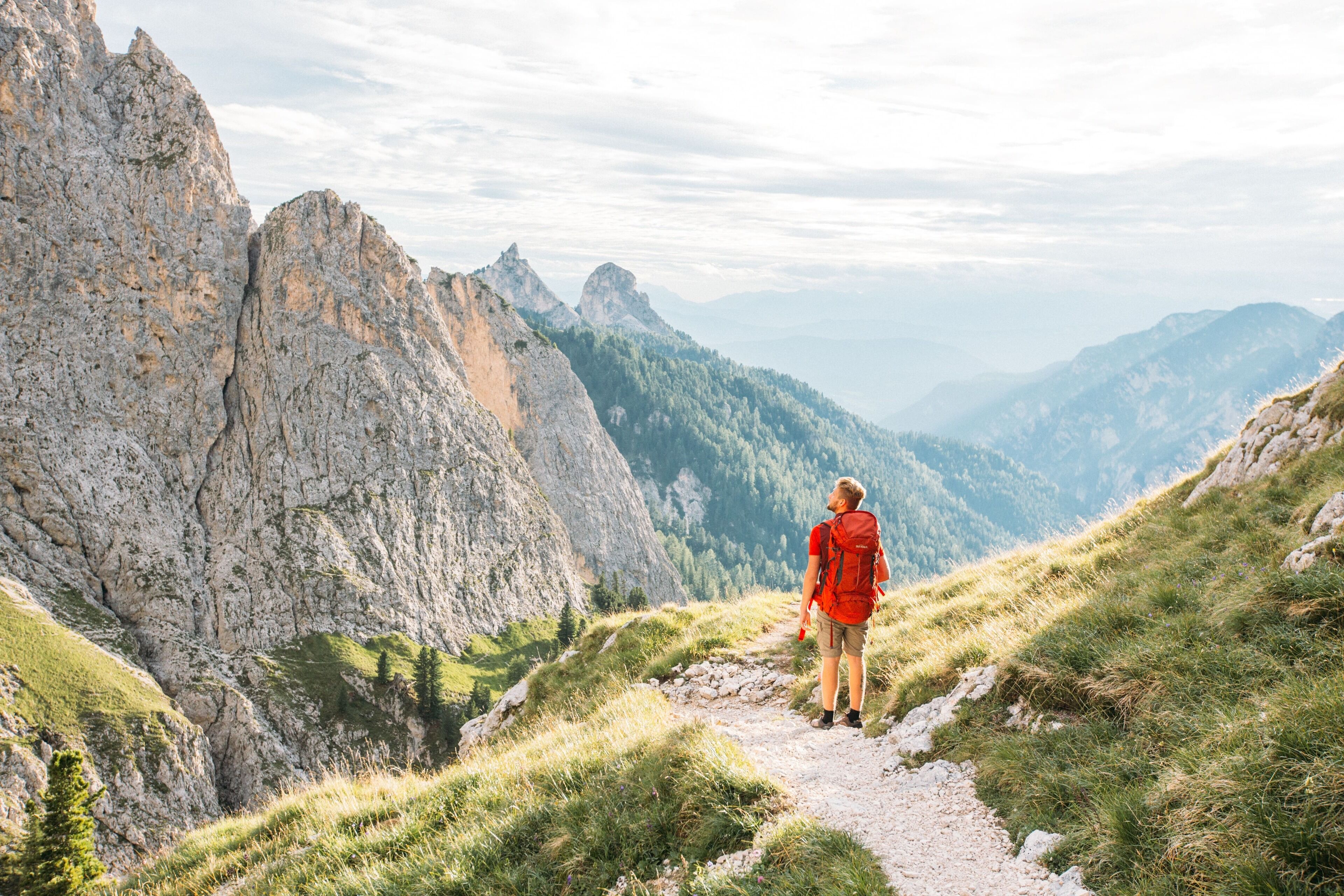 A person hiking on a mountain trail with rocky cliffs and greenery.