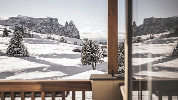 Un balcón de madera con vista a un paisaje montañoso cubierto de nieve.