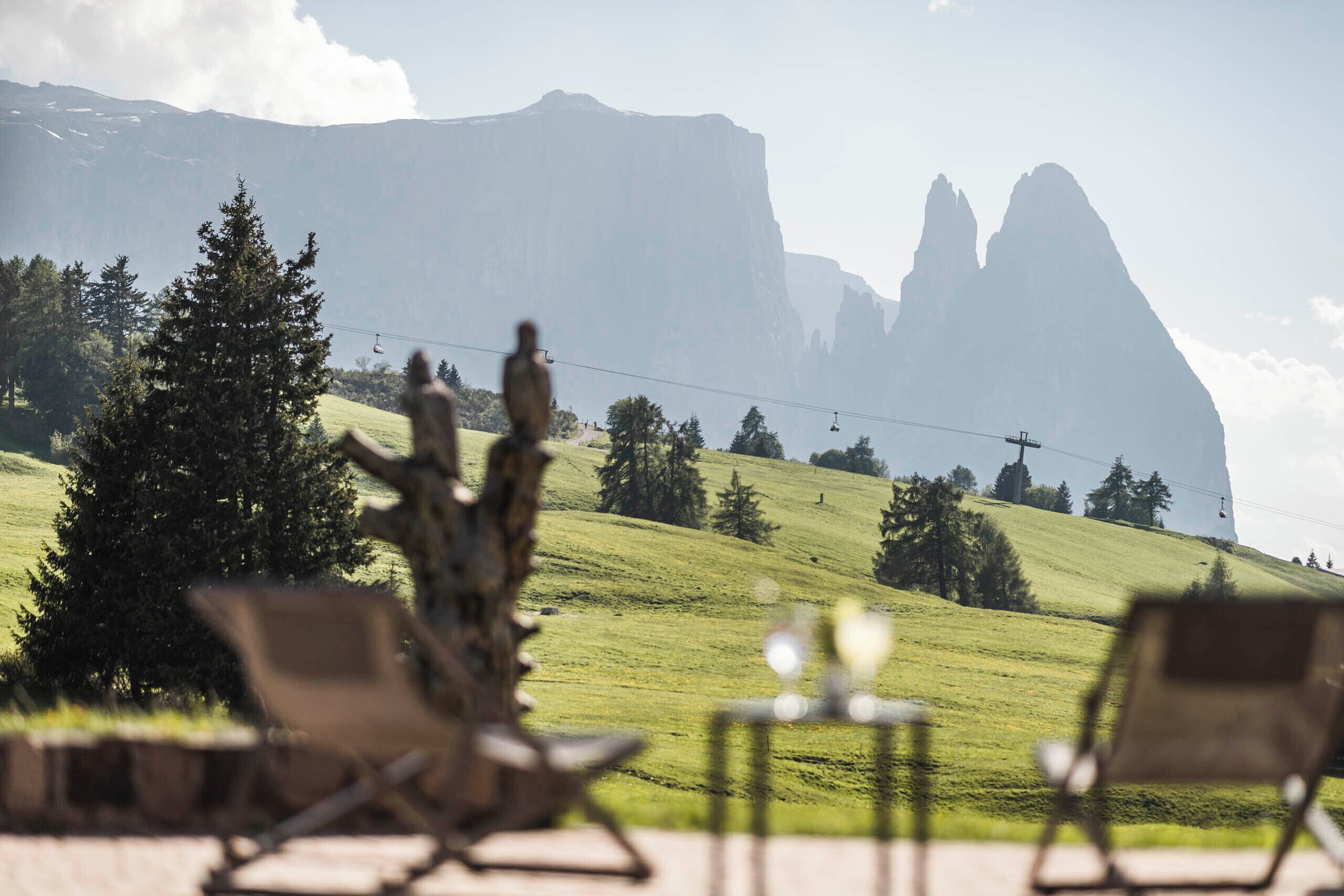 Vista de un paisaje montañoso con una silla y una mesa en primer plano, y un teleférico al fondo.