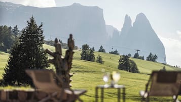 Vista de un paisaje montañoso con una silla y una mesa en primer plano, y un teleférico al fondo.