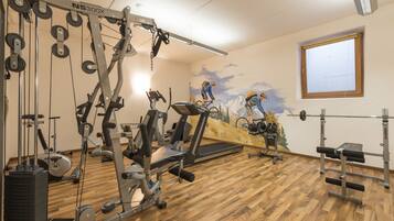 A gym with various exercise equipment, wooden flooring, and a mural of a cyclist on the wall.