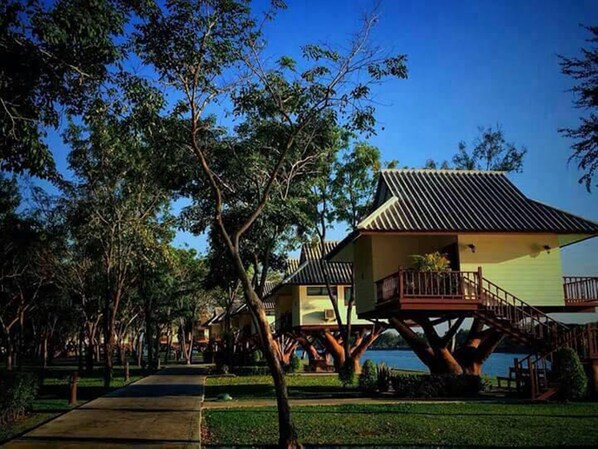 Casas apoyadas en árboles, con un sendero que conduce a una masa de agua.