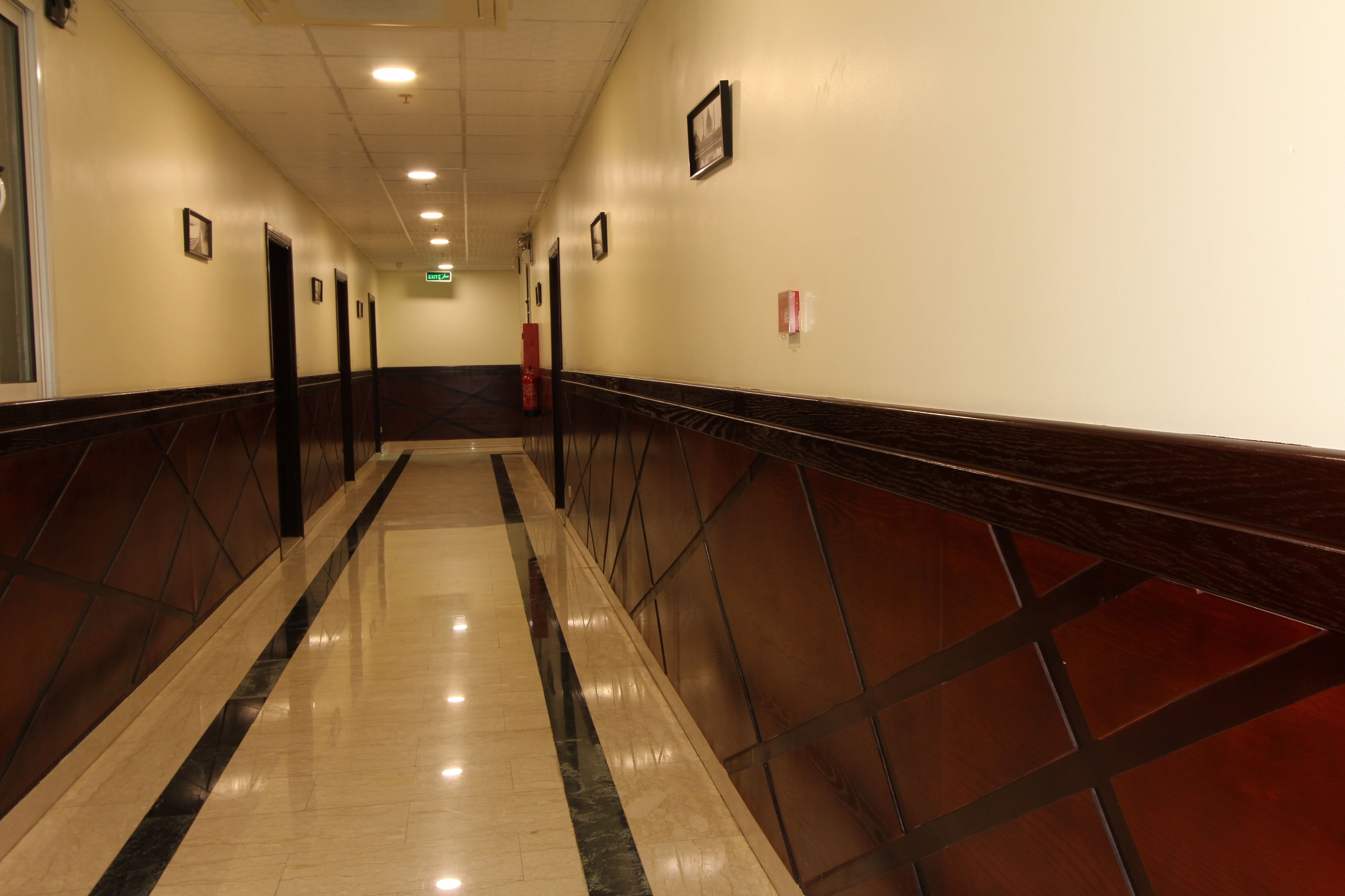 Un pasillo de hotel con piso pulido, paneles de madera oscura y cuadros enmarcados en las paredes.