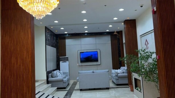 Eine moderne Lobby mit einer Kronleuchter, Einbauleuchten, einem Flachbildfernseher und einer Rezeption.