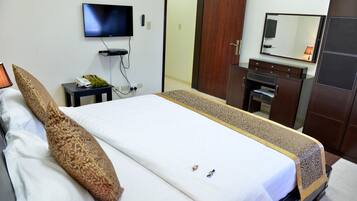 Habitación de hotel con una cama, televisor montado en la pared, una mesita con un teléfono y una planta, y un armario con espejo.