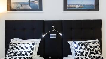 A hotel room with a dark headboard, two beds with matching pillows, a bedside table with a lamp, and two framed pictures on the wall.