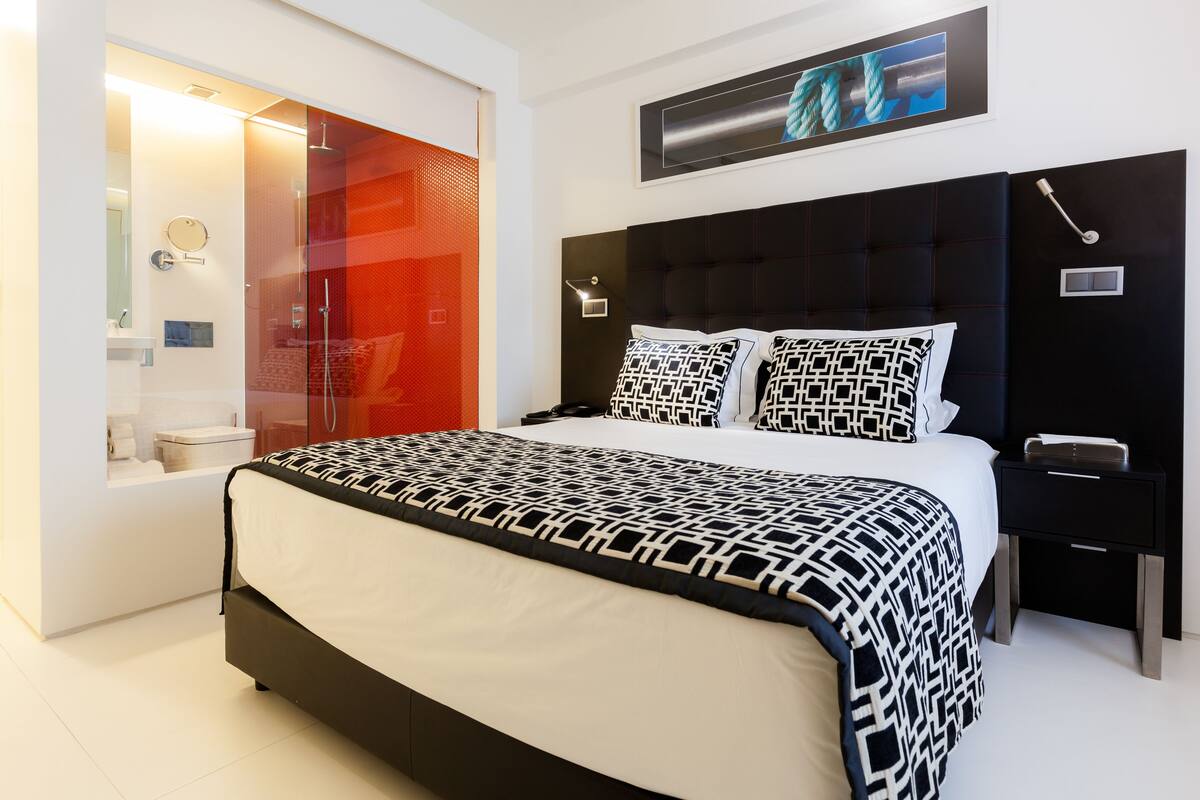 A modern bedroom with a black and white patterned bedspread, a black headboard, and a small bedside table with a lamp.