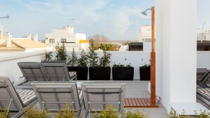 Una terraza en la azotea con sillones de descanso, plantas en macetas y vistas a la ciudad.