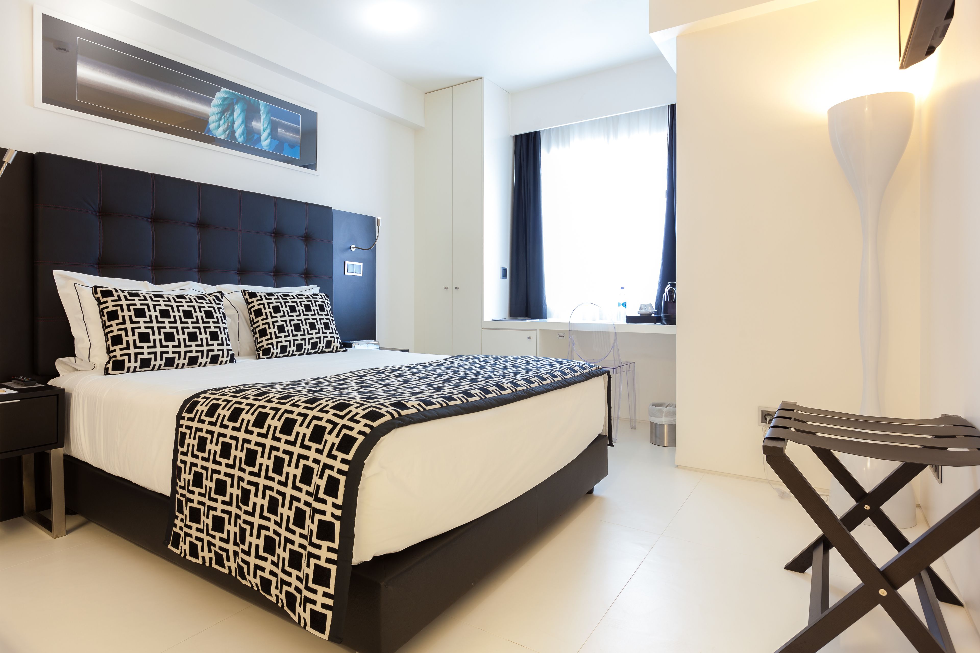 A modern hotel room with a large bed, a desk, and a window with curtains.