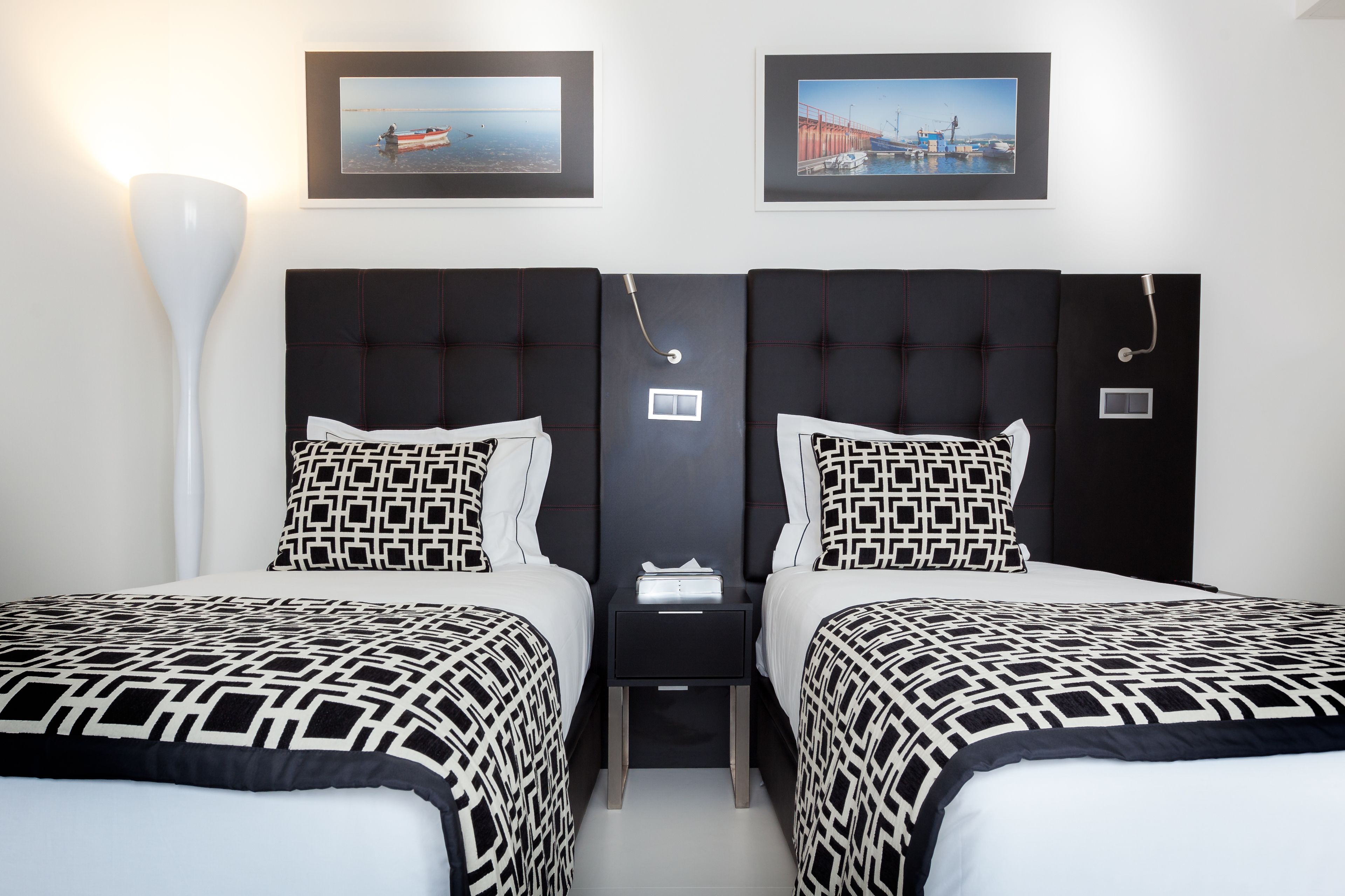 Ein Hotelzimmer mit zwei Betten, jedes mit einer schwarz-weiß gemusterten Tagesdecke, einem Nachttisch zwischen den Betten und zwei gerahmten Bildern an der Wand.